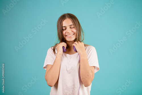 smiling teenager with long straight brown hair and closed eyes is taking off her blue headphones. photo