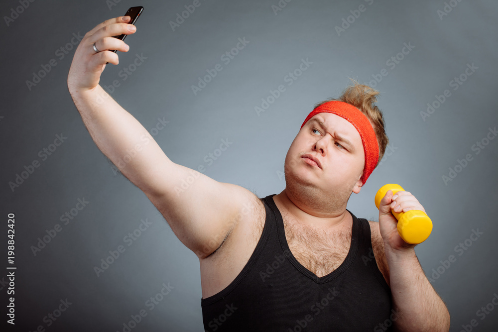 Funny fat man with duck lips wearing black shirt with big belly, holding  dumbbell, doing selfie on grey background Stock Photo | Adobe Stock