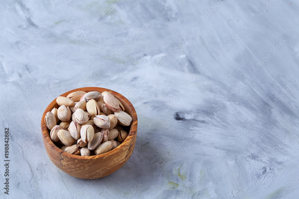 Salted pistachios on a wooden plate over white background, top view, close-up, selective focus. Salted pistachios on a wooden plate over white background, top view, close-up, selective focus.