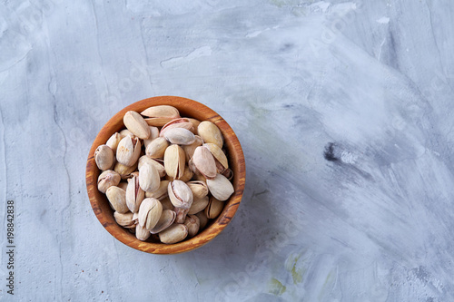 Salted pistachios on a wooden plate over white background, top view, close-up, selective focus. photo