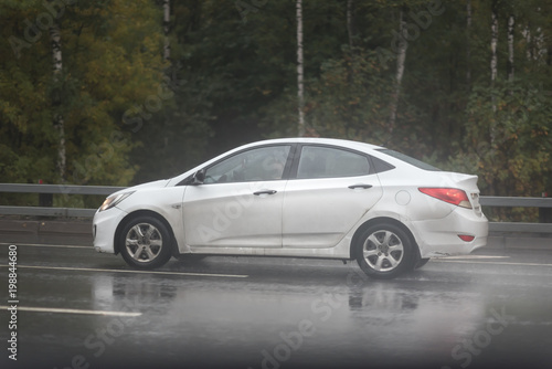 Drive white car in rain on asphalt wet road. Clouds on the sky