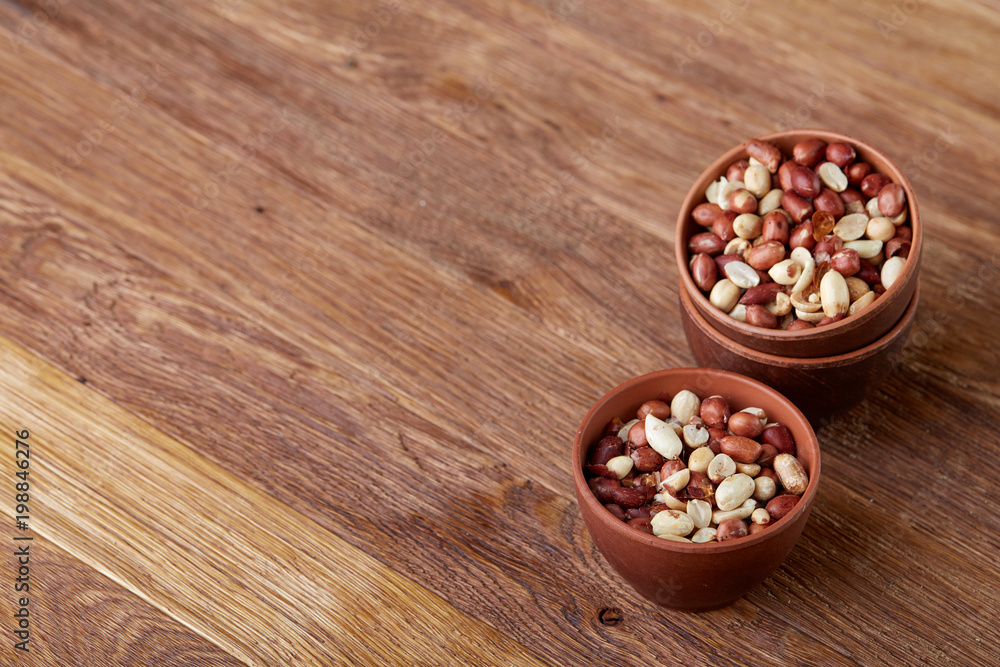 Two ceramic bowls with raw peanuts mix isolated over rustic wooden backround, top view, close-up.