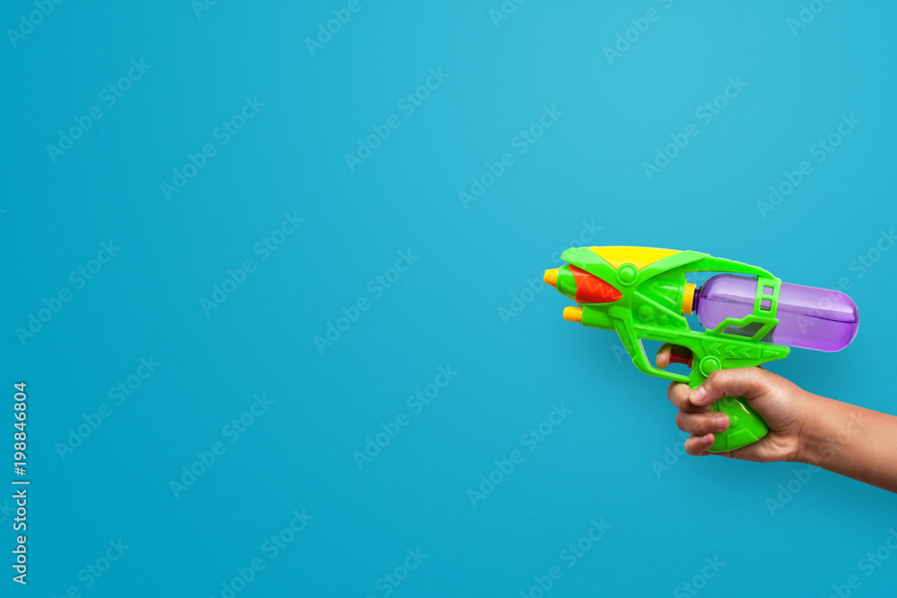 Hand holding plastic water gun on blue background. Objects with