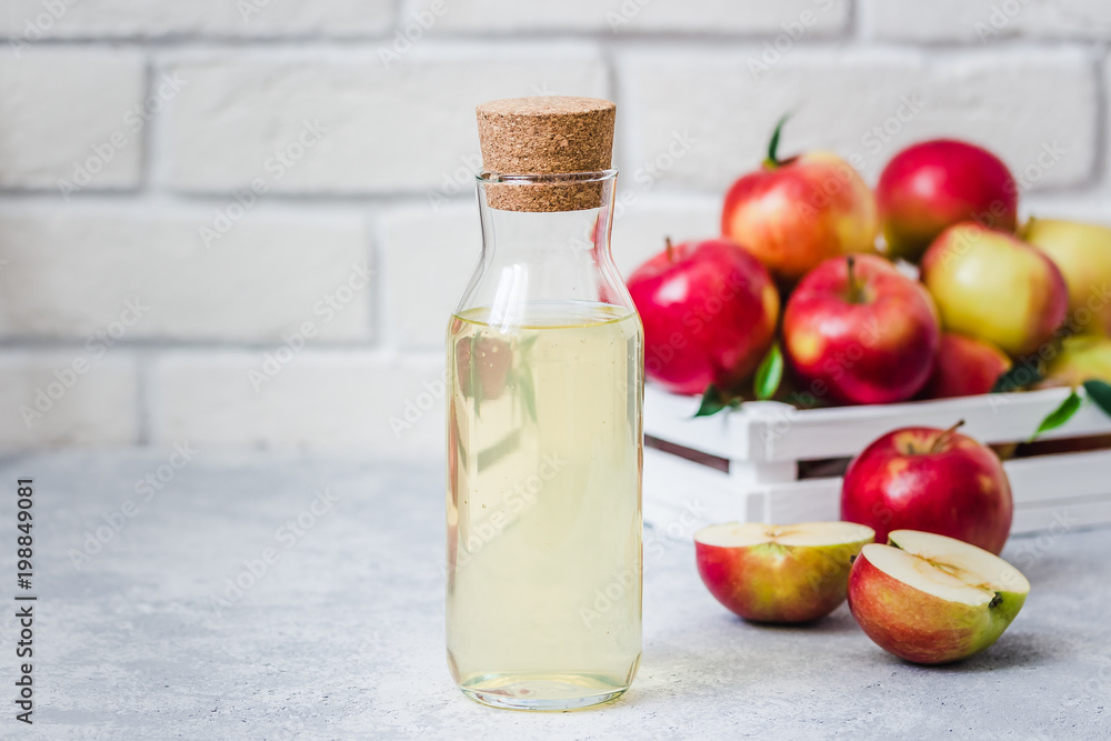 Fermented apple cider and fresh red apples in white wooden box on light background. Selective focus, space for text. Fermented apple cider and fresh red apples in white wooden box on light background. Selective focus, space for text.