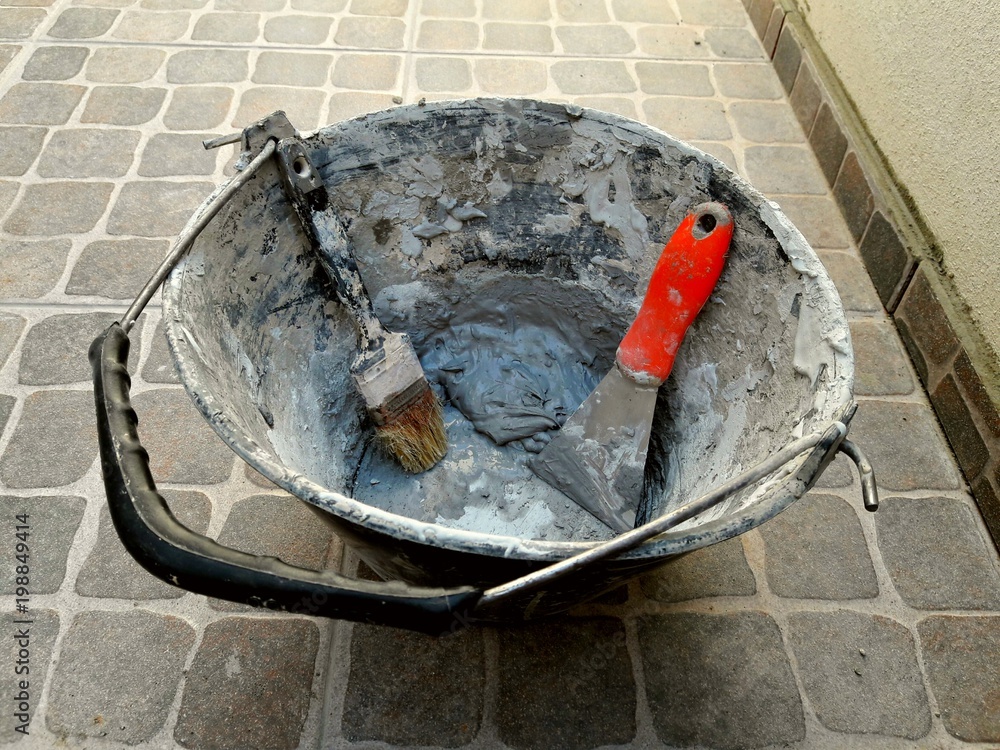 Espátula, pincel y balde de construcción usados y gastados sobre piso adoquín