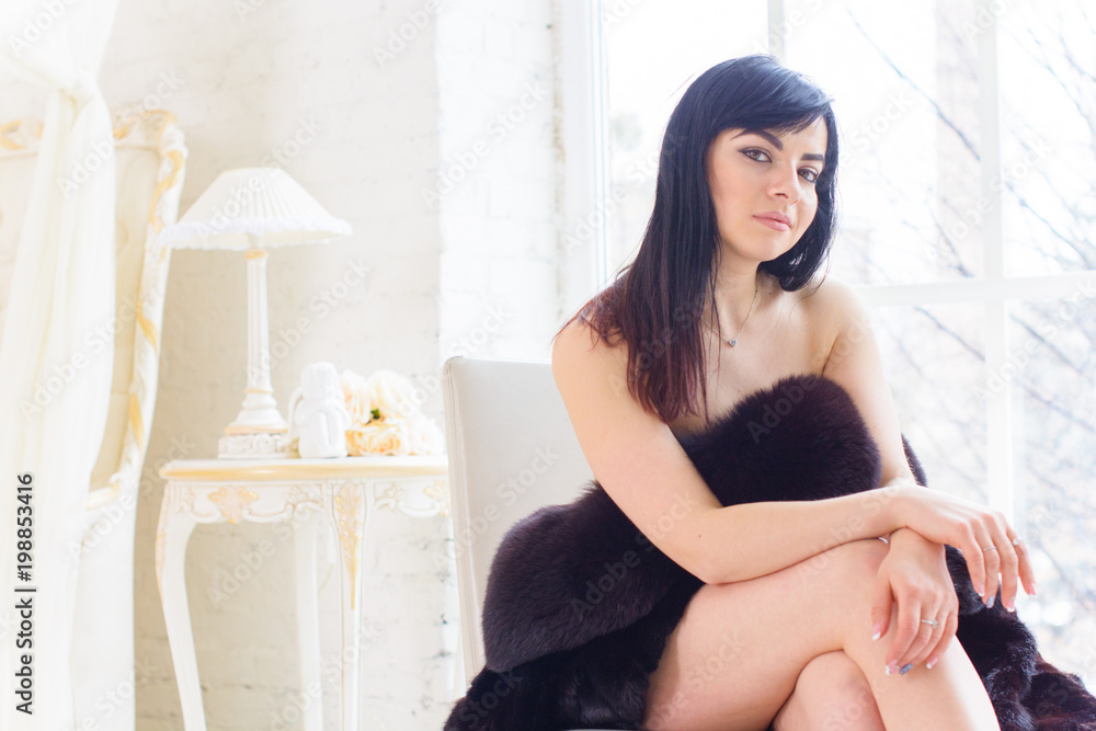 Obraz premium Sensual latin naked woman in white interior, relaxing at cozy hotel. Portrait of a beautiful woman wearing fur 