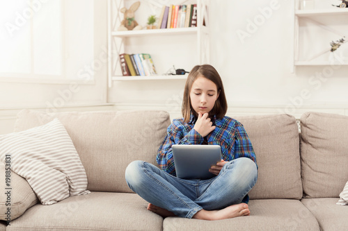 Pensive girl with digital tablet at home