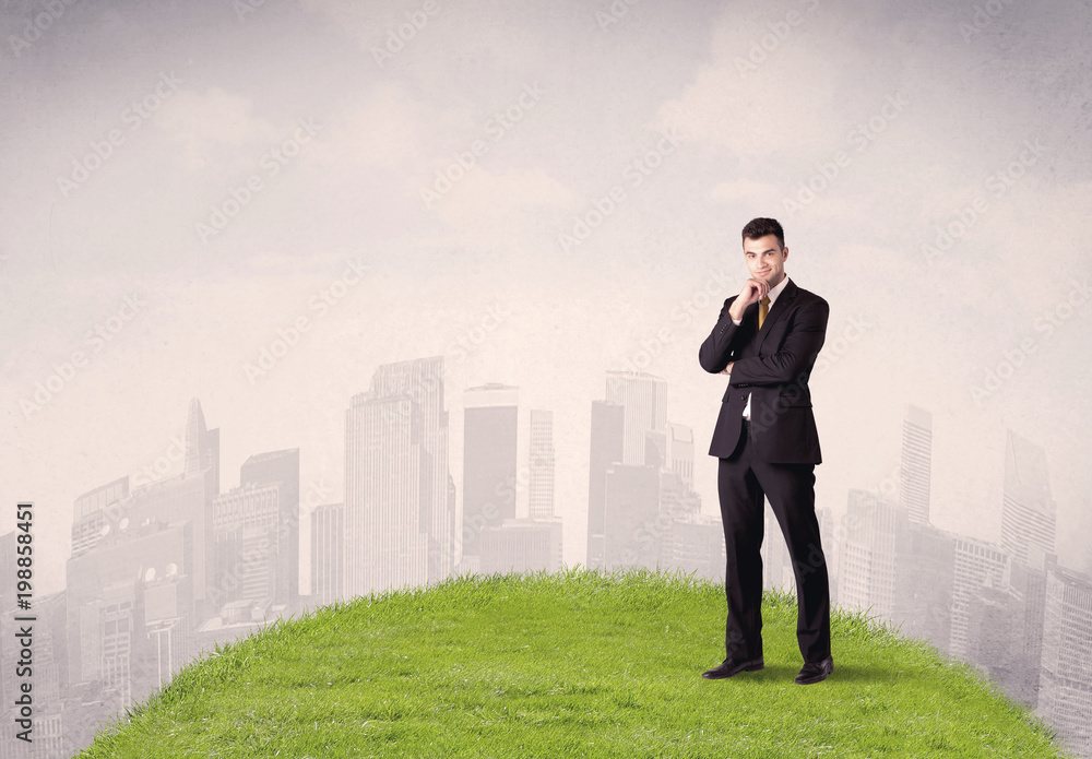 A confident male well looking office manager standing in small green grass in front of city landscape with tall buildings concept.