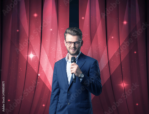 Businessman speaking into microphone with red curtain behind him 