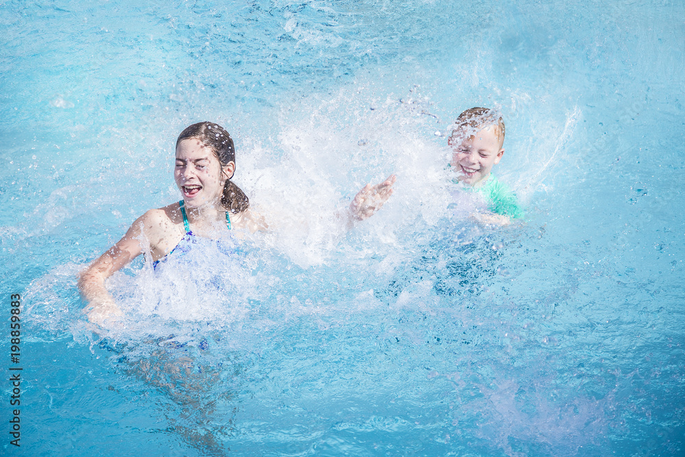 Two cute kids laughing and splashing each other in the swimming pool while on a summer vacation . Water is splashing everywhere and kids are having lots of fun