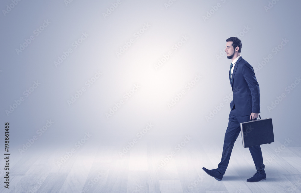 Successful businessman walking in front of an empty wall with briefcase on his hand
Successful businessman walking in front of an empty wall with briefcase on his hand