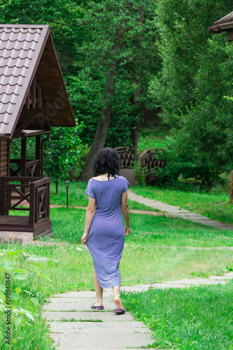 A sexy girl in a tight sea dress, walking along a stone path, a back view. summer photo