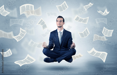 Young businessman meditating with documents and papers flying around him
