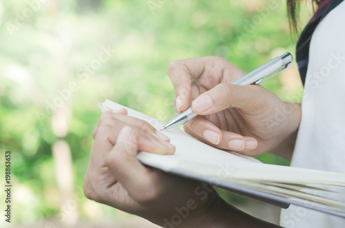 attractive woman using the pencil writing on daily notebook paper at outdoor in the park.