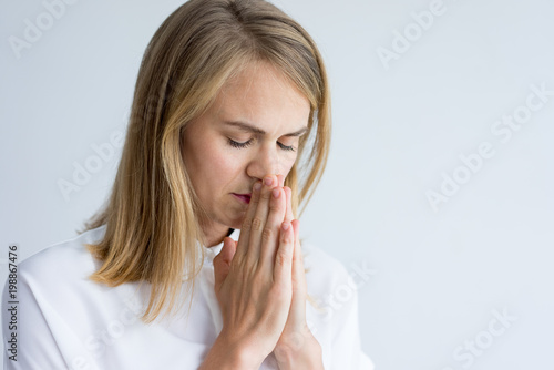 Portrait of concentrated young Caucasian woman wearing white shirt praying. Young business assistant with closed eyes thinking how to solve problem. Spirituality, concentration concept