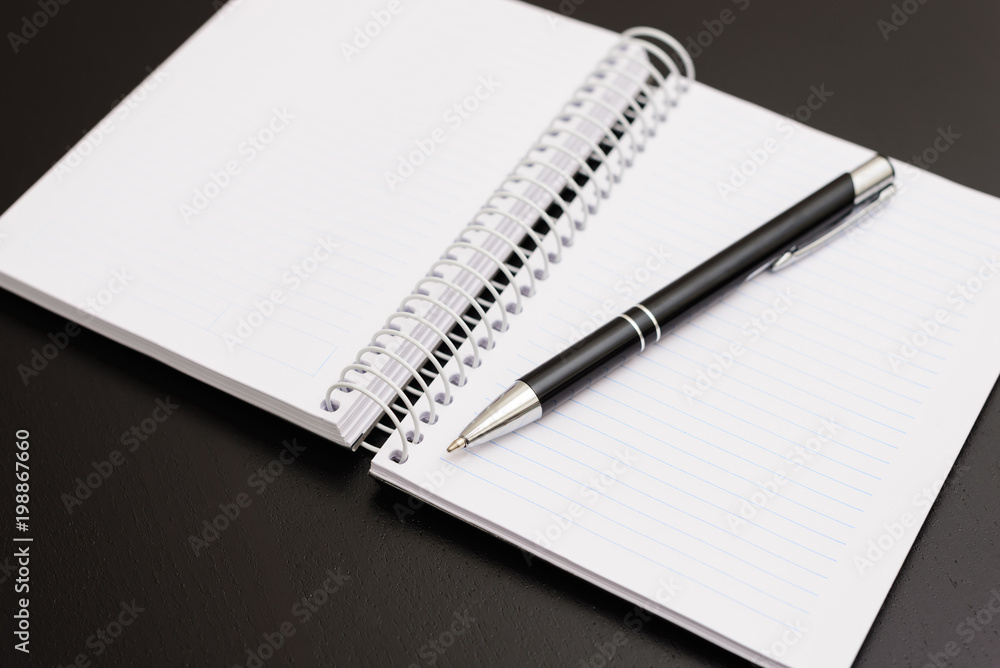 Notepad and pen on black wooden table. Objects very used for small work and notes. Notepad and pen on black wooden table. Objects very used for small work and notes.
