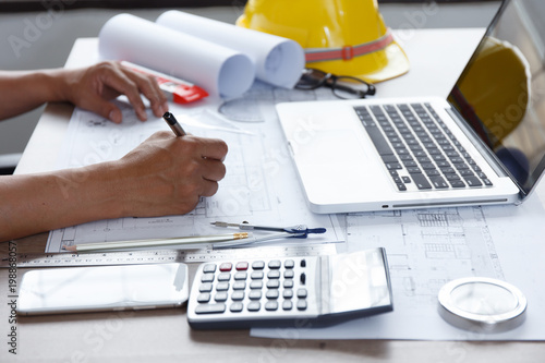 Top view, Architect or engineer hands working on blueprint plans with a pencil ,laptop a ruler, calculator, and engineering tools. Architect or engineer working on blueprint in office.