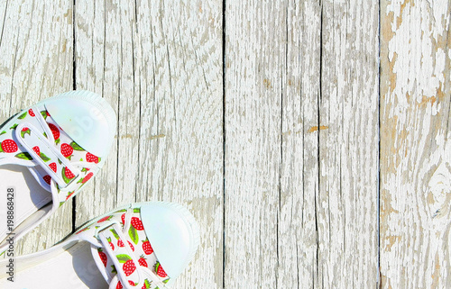 White with red berries sneakers on a white wooden background. Summer shoes top view. Colored slippers stand on old painted boards. Free space for text.