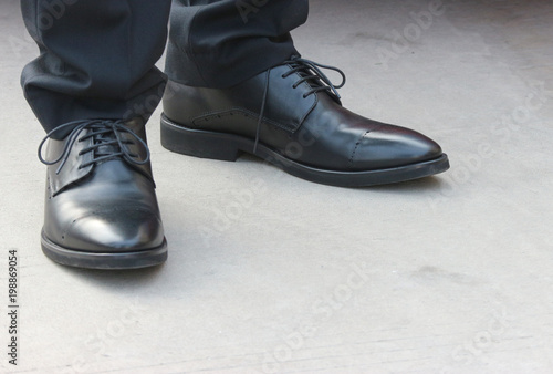 A Business man wear a black leather shoes and standing on cement road floor.