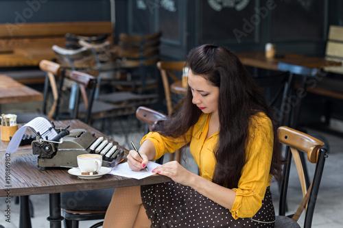 Female writer with vintage typewriter taking notes in a coffee s