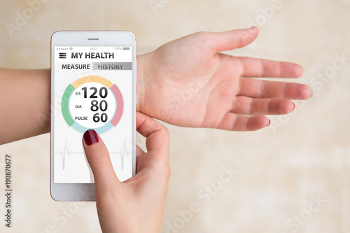 Woman measures blood pressure and pulse by mobile phone with medical application photo