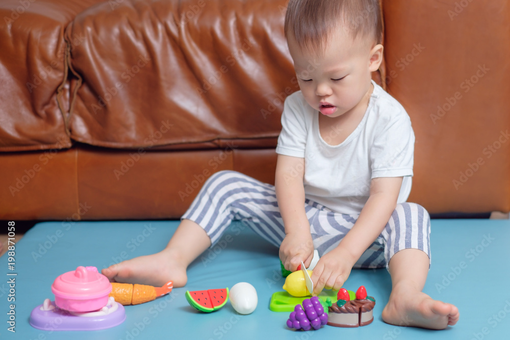 Cute little Asian 18 months / 1 year old toddler boy child sitting on floor near sofa in living room at home having fun playing alone with cooking toys , Educational toys for young children concept Cute little Asian 18 months / 1 year old toddler boy child sitting on floor near sofa in living room at home having fun playing alone with cooking toys , Educational toys for young children concept