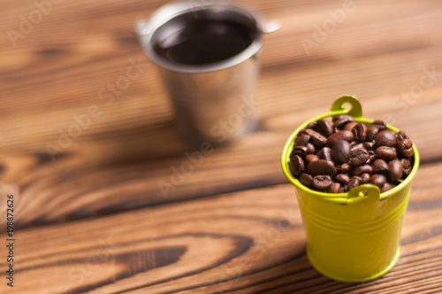 Full zinked bucket of black coffee near green metal bucket with handle full of roasted coffee beans on old worn wooden table photo