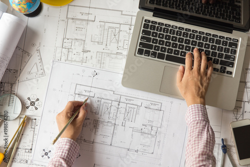 Architect or engineer hands working on blueprint plans  with  a pencil and laptop  a ruler, calculator,  and engineering tools.    Architect or engineer working on blueprint in office. 