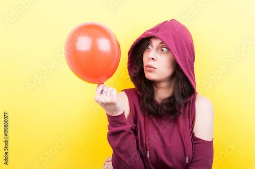 Woman making silly faces with a ballon in hands on yellow background in studio