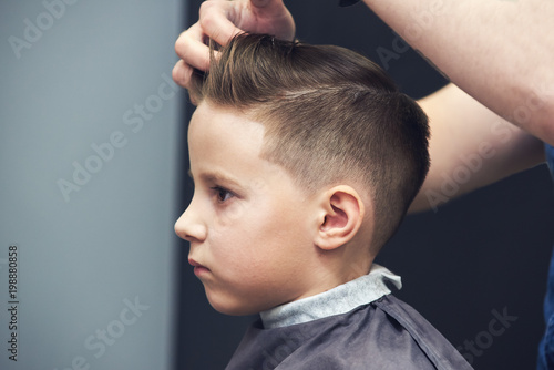 Barber making hairstyle to a Caucasian boy using hair gel.