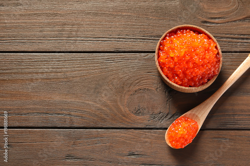 Spoon and bowl with delicious red caviar on wooden background