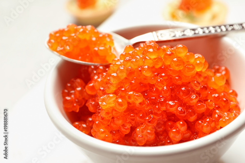 Spoon and bowl with delicious red caviar on light background, closeup
