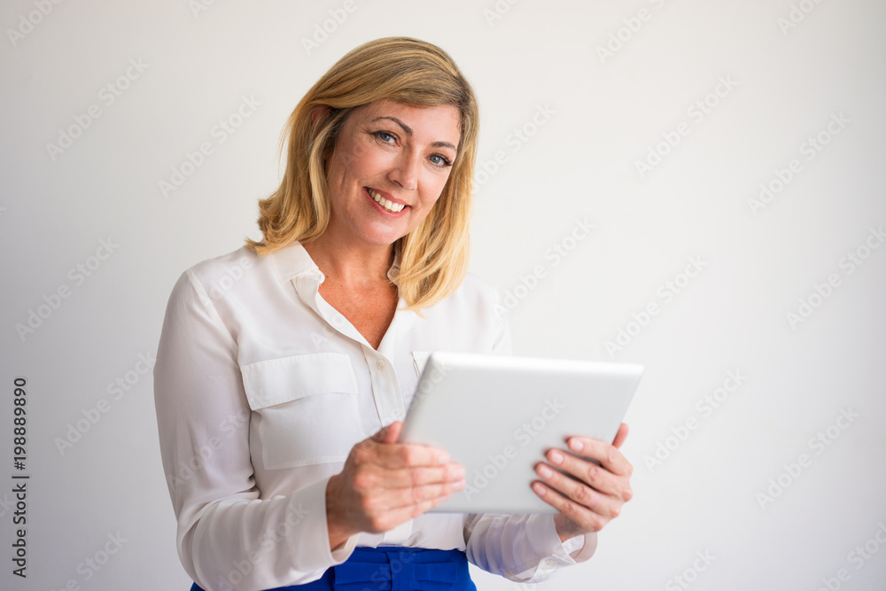 Φωτογραφία Closeup portrait of smiling middle-aged attractive fair-haired woman looking at camera and using tablet computer