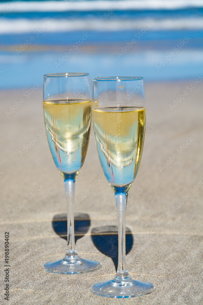 Two glasses of champagne or cava sparkling wine served on the white sandy tropical beach, luxury resort with sea view, romantic vacation Two glasses of champagne or cava sparkling wine served on the white sandy tropical beach, luxury resort with sea view, romantic vacation