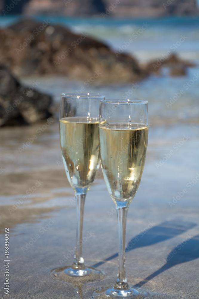 Two glasses of champagne or cava sparkling wine served on the white sandy tropical beach, luxury resort with sea view, romantic vacation