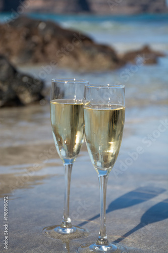 Two glasses of champagne or cava sparkling wine served on the white sandy tropical beach, luxury resort with sea view, romantic vacation