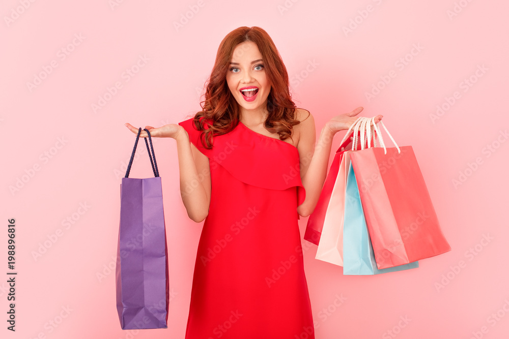 Young woman studio isolated on pink in a red dress holding shopping bags
