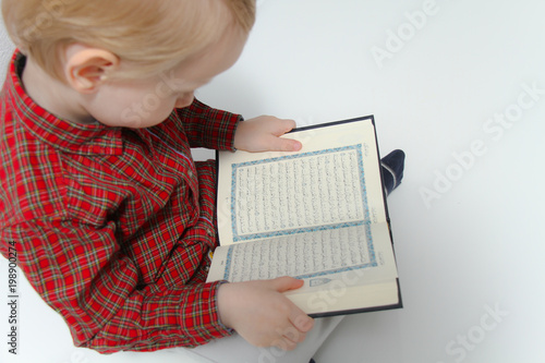 Little muslim European boy with islamic holy book Quran or Kuran photo