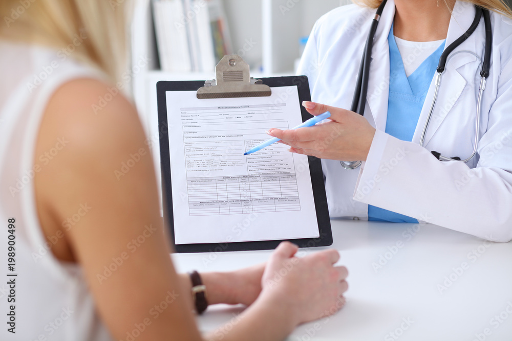 Close up of a doctor and patient hands while phisician pointing into medical history form at clipboard Close up of a doctor and patient hands while phisician pointing into medical history form at clipboard