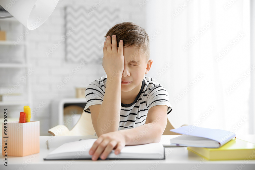 Little boy suffering from headache while doing homework at table indoors Little boy suffering from headache while doing homework at table indoors