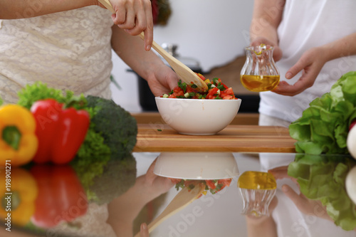 Closeup of human hands cooking in kitchen. Mother and daughter or two female friends mixing salad of vegetables. Healthy meal, vegetarian food and lifestyle concepts