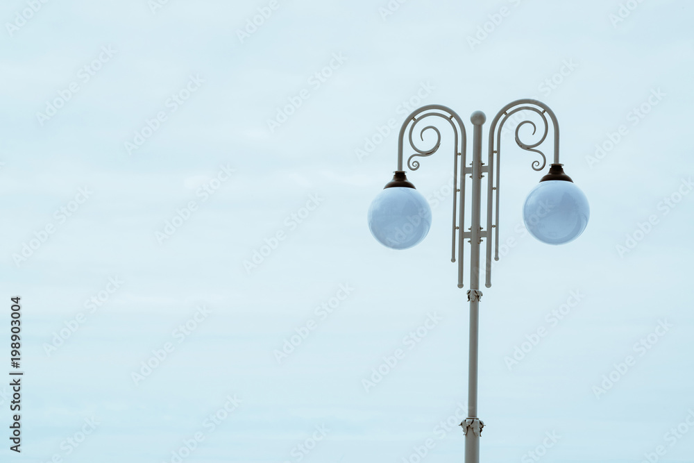 White pillar in vintage style with double suspended lantern in sphere form on blue sky background. Streetlight.