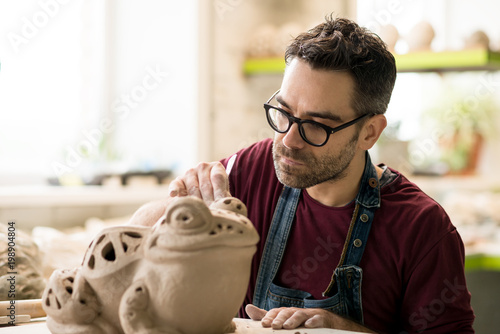 Ceramist Dressed in an Apron Sculpting Statue from Raw Clay in Bright Ceramic Workshop. photo