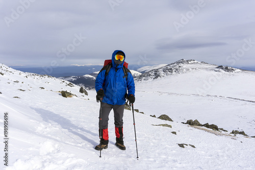 mountaineer in mirror wind-proof glasses and a windproof mask with a backpack on a background of a winter mountain landscape