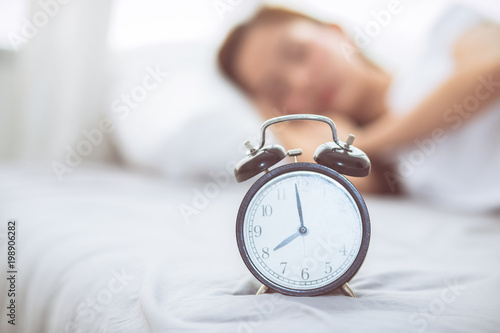 Beautiful asian young woman turn off alarm clock in good morning, wake up for sleep with closeup foreground alarm clock, relax and lifestyle concept.