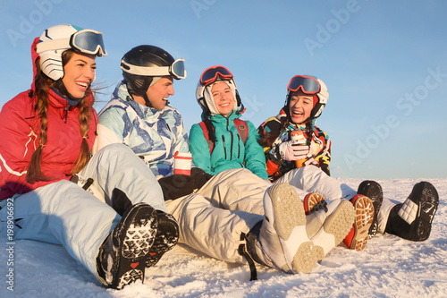 Happy friends sitting on snowy mountain peak at ski resort. Winter vacation