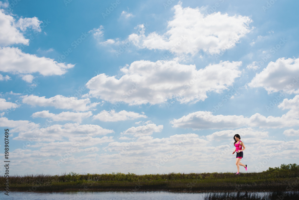 Running girl on a green field and bright sky