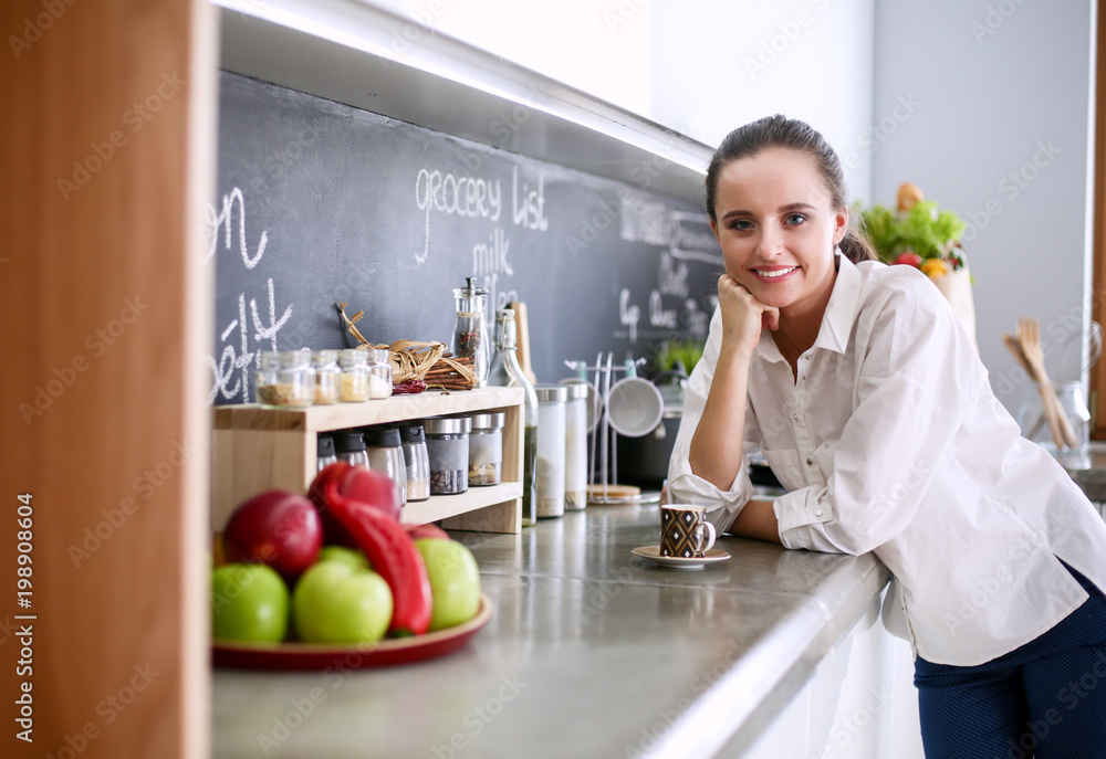 Portrait of young woman standing against kitchen background. Portrait of young woman standing against kitchen background.