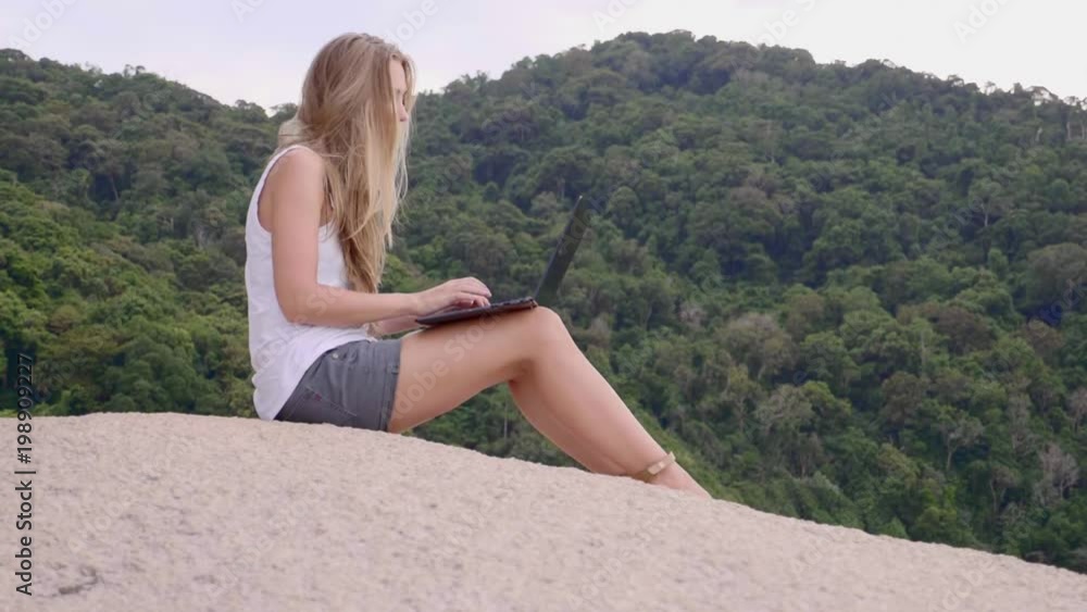 Business woman using laptop computer on top of the mountain with a view over white sand beach. Vacation, freelance job, leisure activity concept. Business woman using laptop computer on top of the mountain with a view over white sand beach. Vacation, freelance job, leisure activity concept.