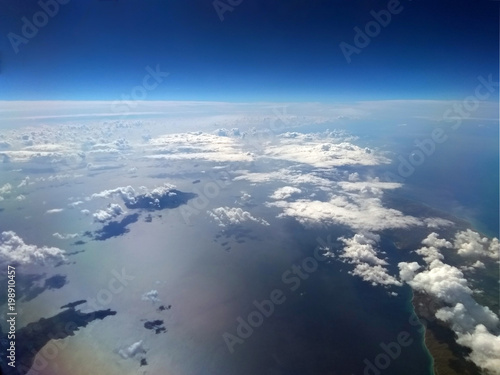 high altitude image of the earth with blue sky and white clouds over the sea with sun reflected on the water and small islands